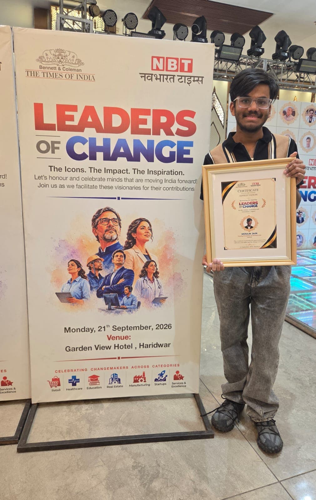 Moulik Jain holding his Leaders of Change 2026 certificate beside the event banner dated 21 September 2026 at Garden View Hotel, Haridwar